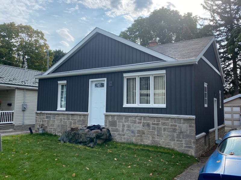 Charcoal board and batten aluminum siding on a bungalow with stone skirt in Kitchener
