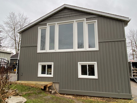 Dark brown vertical board and batten siding on a two-storey garage with white windows