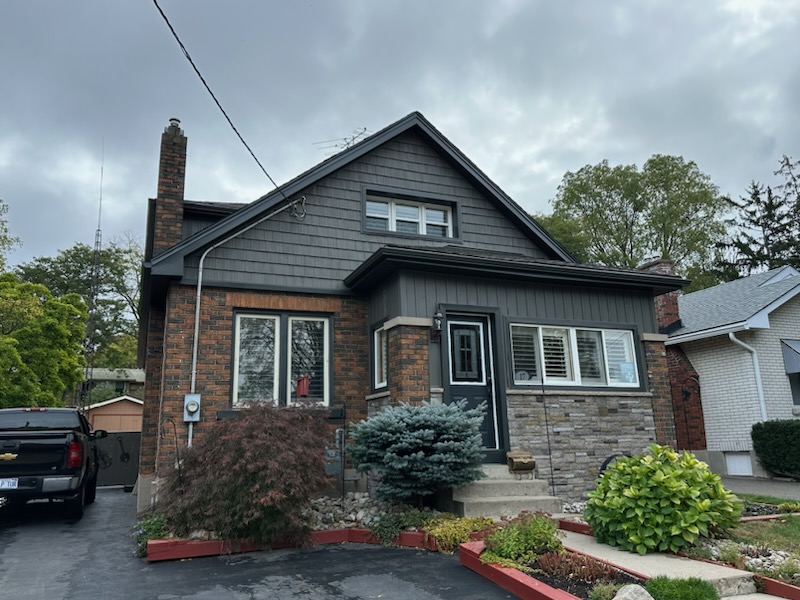 Dark grey vinyl shake and board and batten siding on a brick storey-and-a-half home