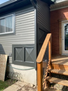 Grey siding with dark board and batten crawl space access door beside a wood deck